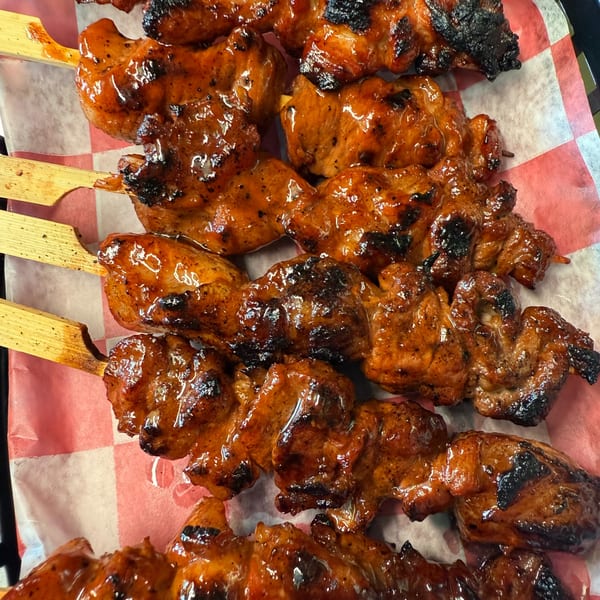 Close-up of several glistening, grilled BBQ chicken skewers on red and white checkered paper.