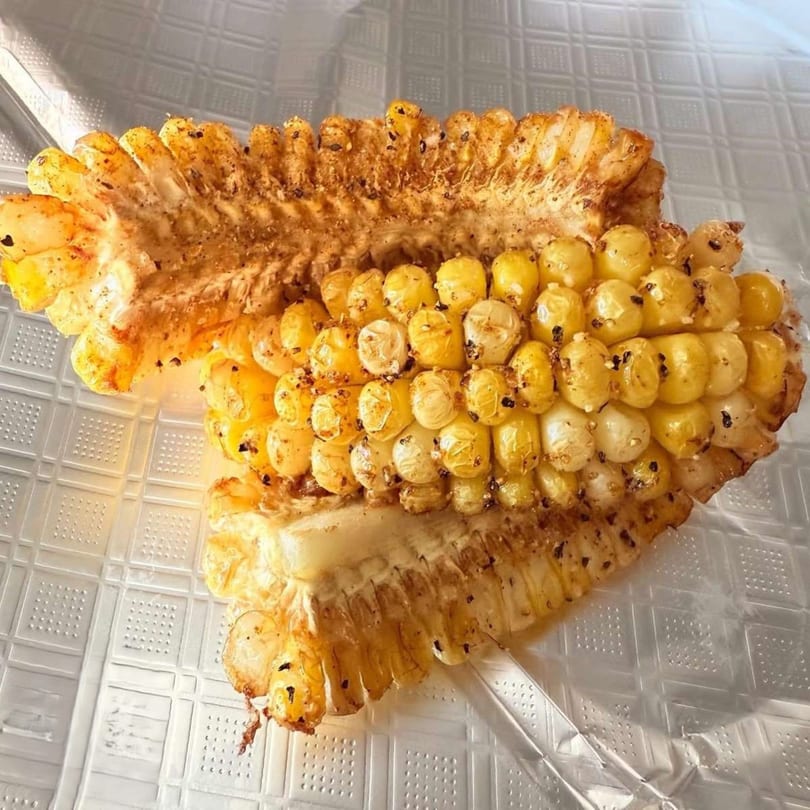 A half-eaten cob of grilled corn, seasoned with spices, on a clear textured surface.