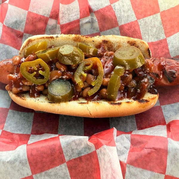 Duffy's BBQ hot dog with baked beans and sliced jalapeños on checkered paper.