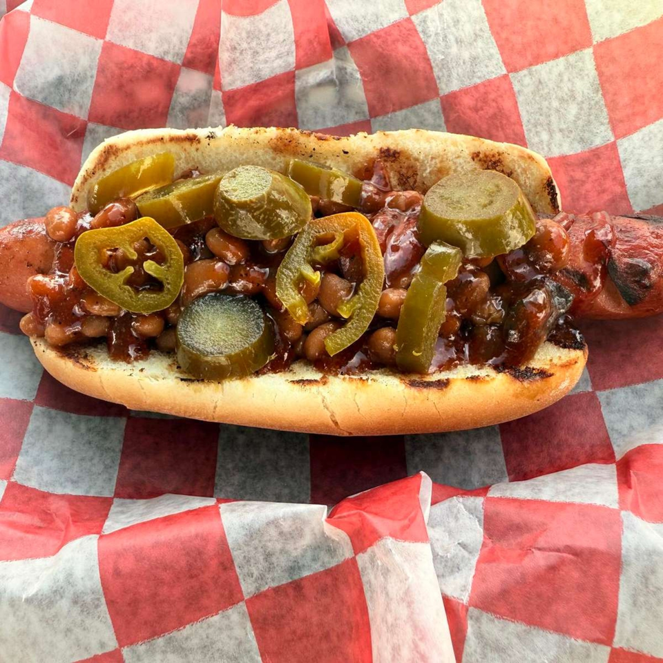 Duffy's BBQ hot dog with baked beans and sliced jalapeños on checkered paper.