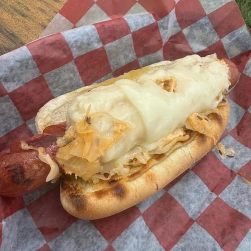 A grilled hot dog with melted cheese and caramelized onions on a bun, on checkered paper.