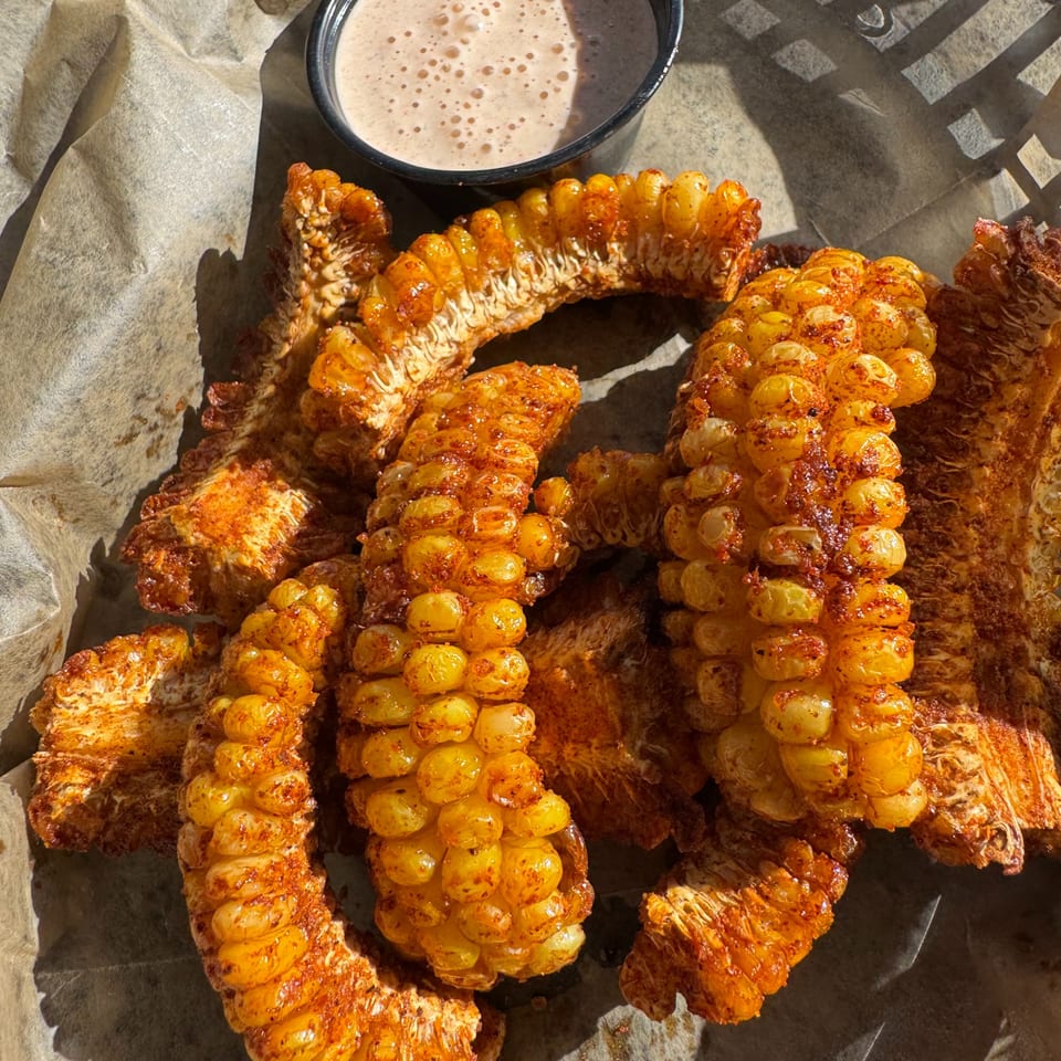 Close-up of BBQ corn ribs with seasoning and a side of dipping sauce in a basket.