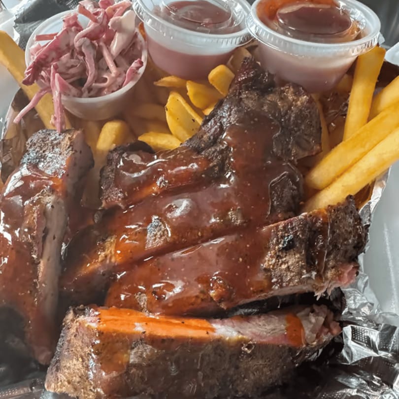 Duffy's BBQ ribs with fries, coleslaw, and dipping sauces in a foil-lined container.