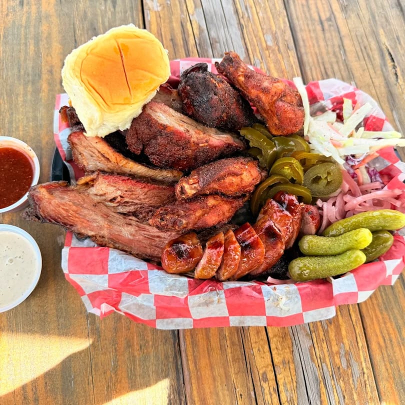 Duffy's BBQ platter with ribs, chicken, sausage, coleslaw, pickles, and jalapeños on a wooden table.