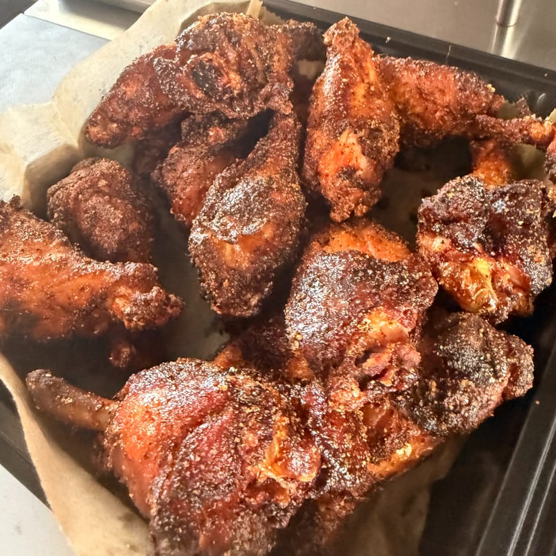 Close-up of crispy, seasoned BBQ chicken wings in a black tray lined with parchment paper.