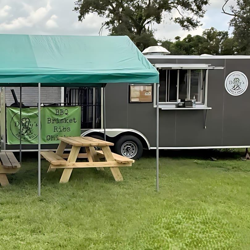 Duffy's BBQ and Grill food truck with a green tent and picnic tables on a grassy field.